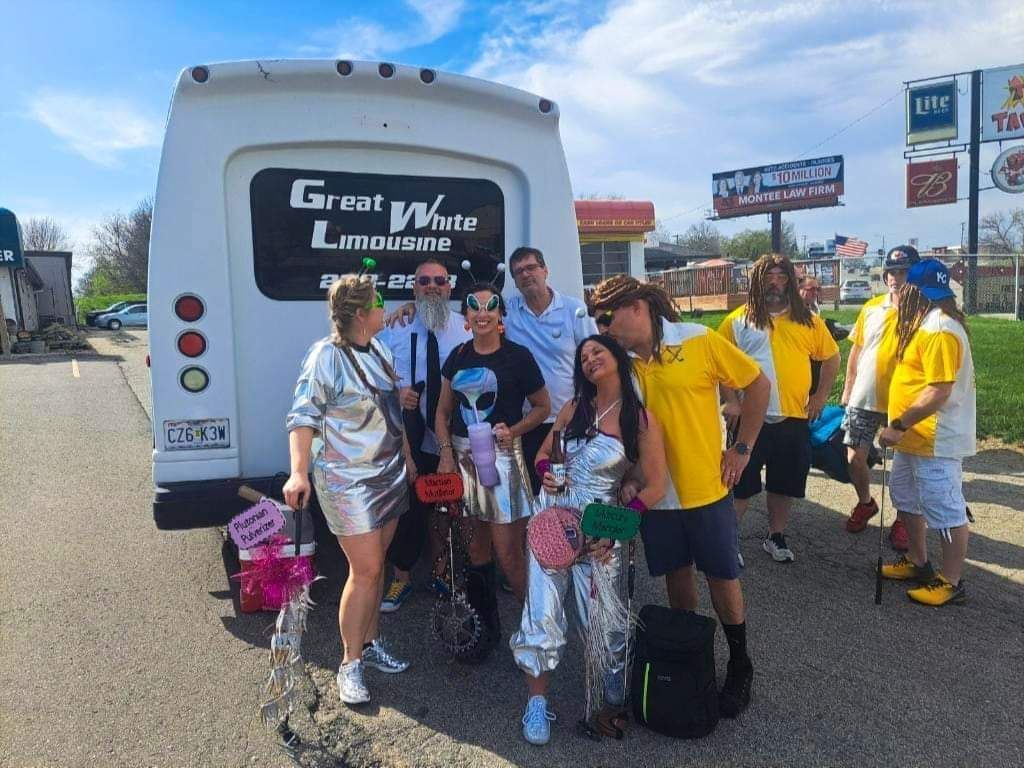 Group of people with bags posing beside a Great White Limo bus on a sunny day.