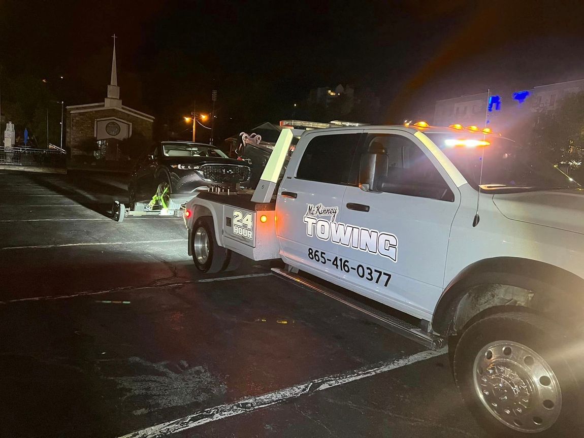 A white tow truck is parked in a parking lot at night.