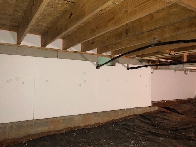 A basement under construction with a white wall and wooden beams