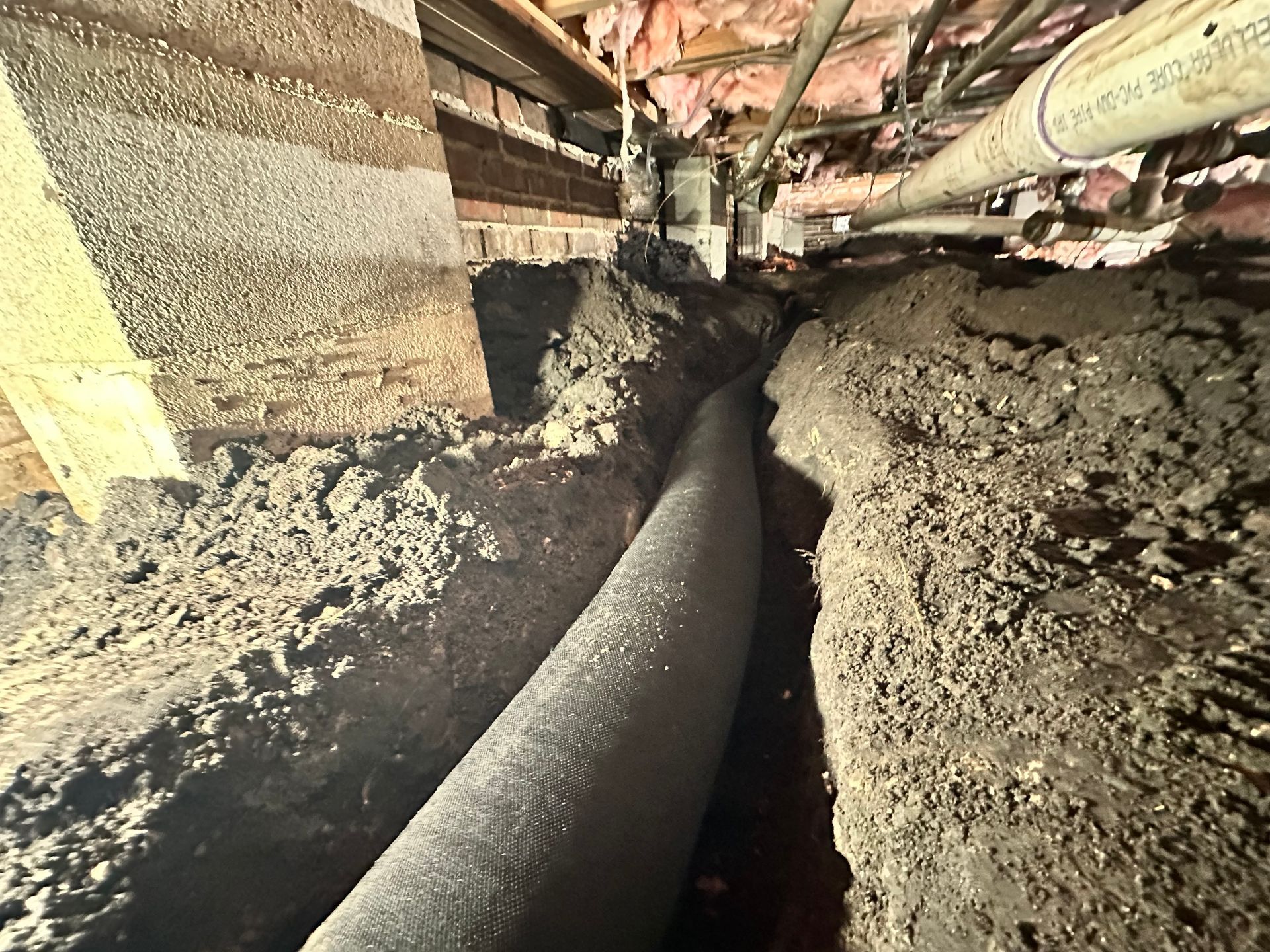 A pipe is laying in the dirt under a house.