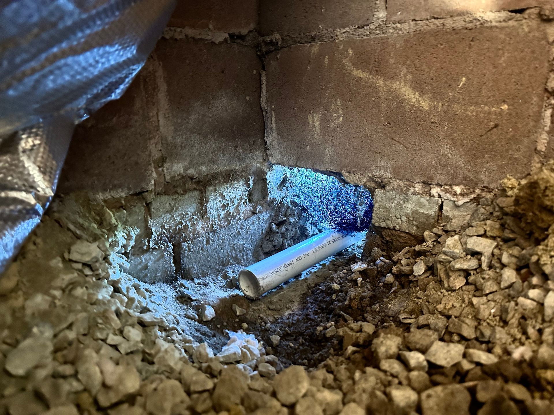 A pipe is sticking out of a hole in a brick wall.