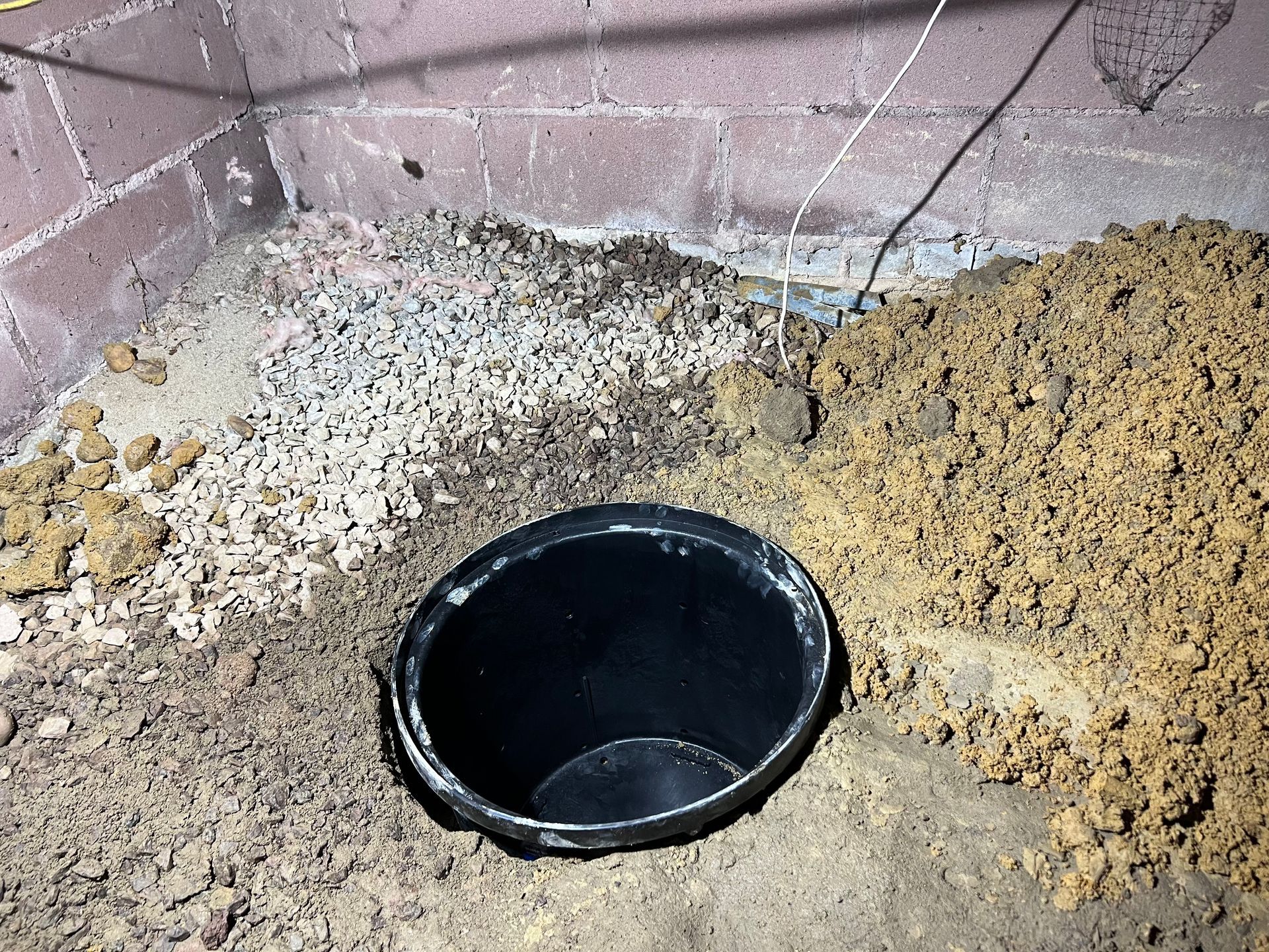 A black bucket is sitting in the middle of a pile of dirt.