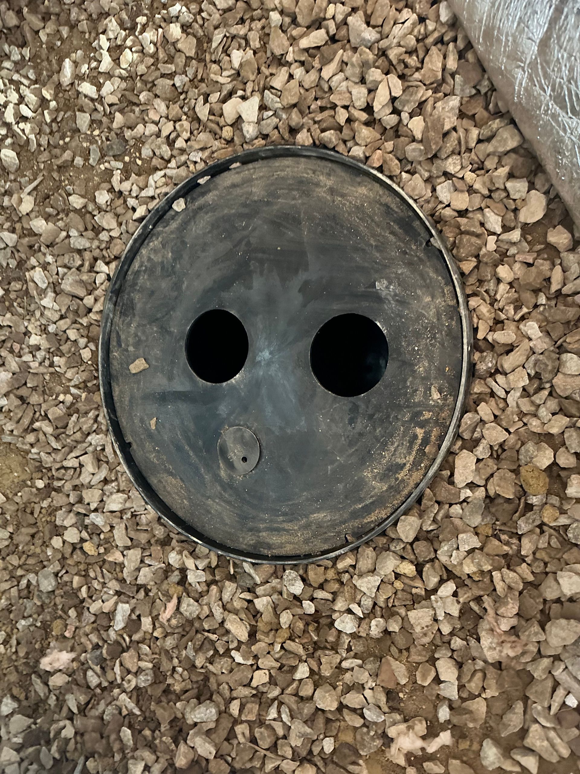 A round object with two holes in it is sitting on a pile of gravel.