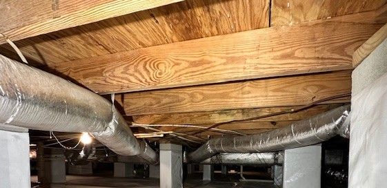 A basement with wooden beams and ducts coming out of the ceiling.
