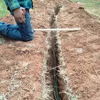 A person is kneeling down in the dirt next to a hose.