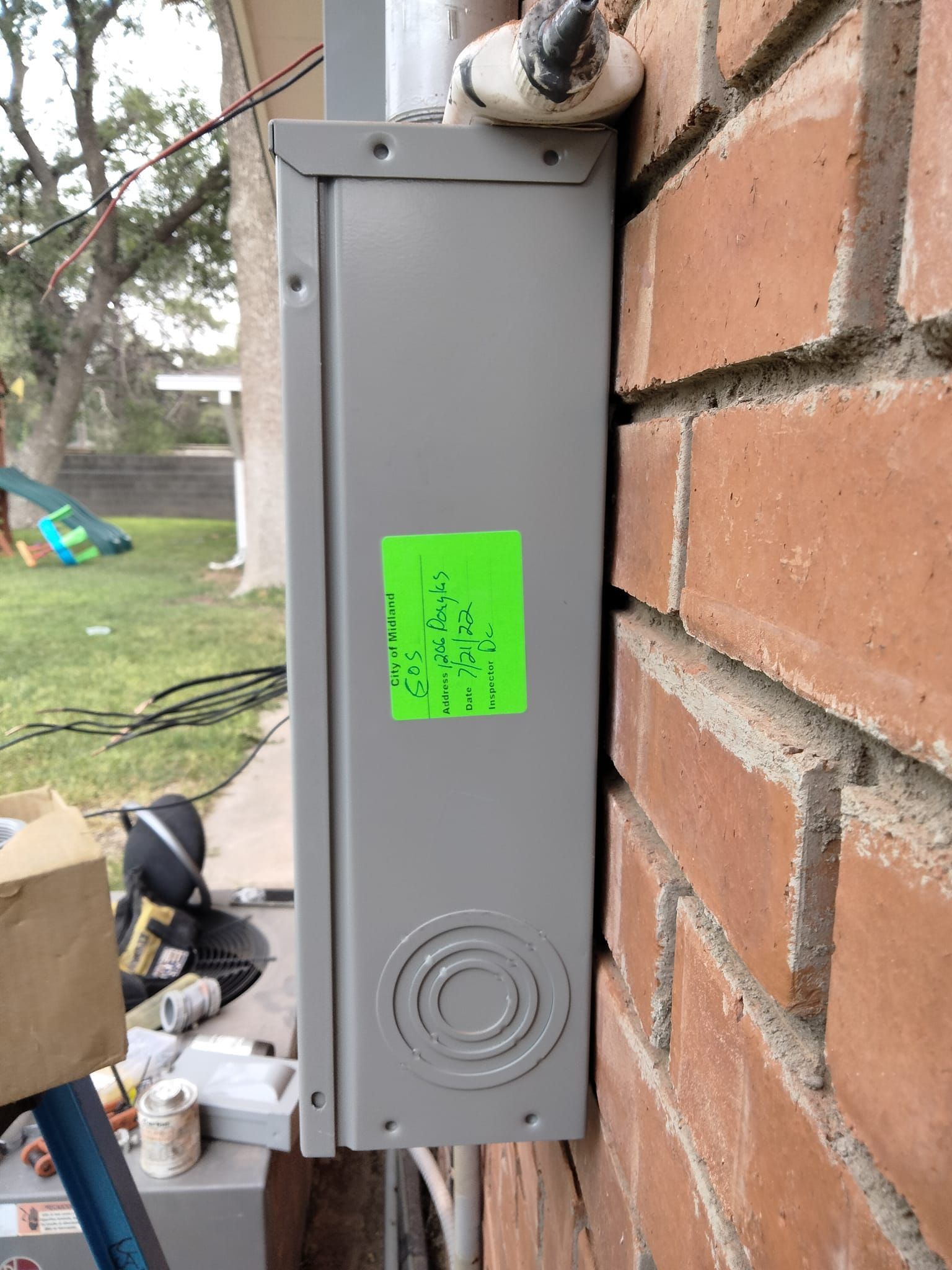 A gray box with a green sticker on it is attached to a brick wall.
