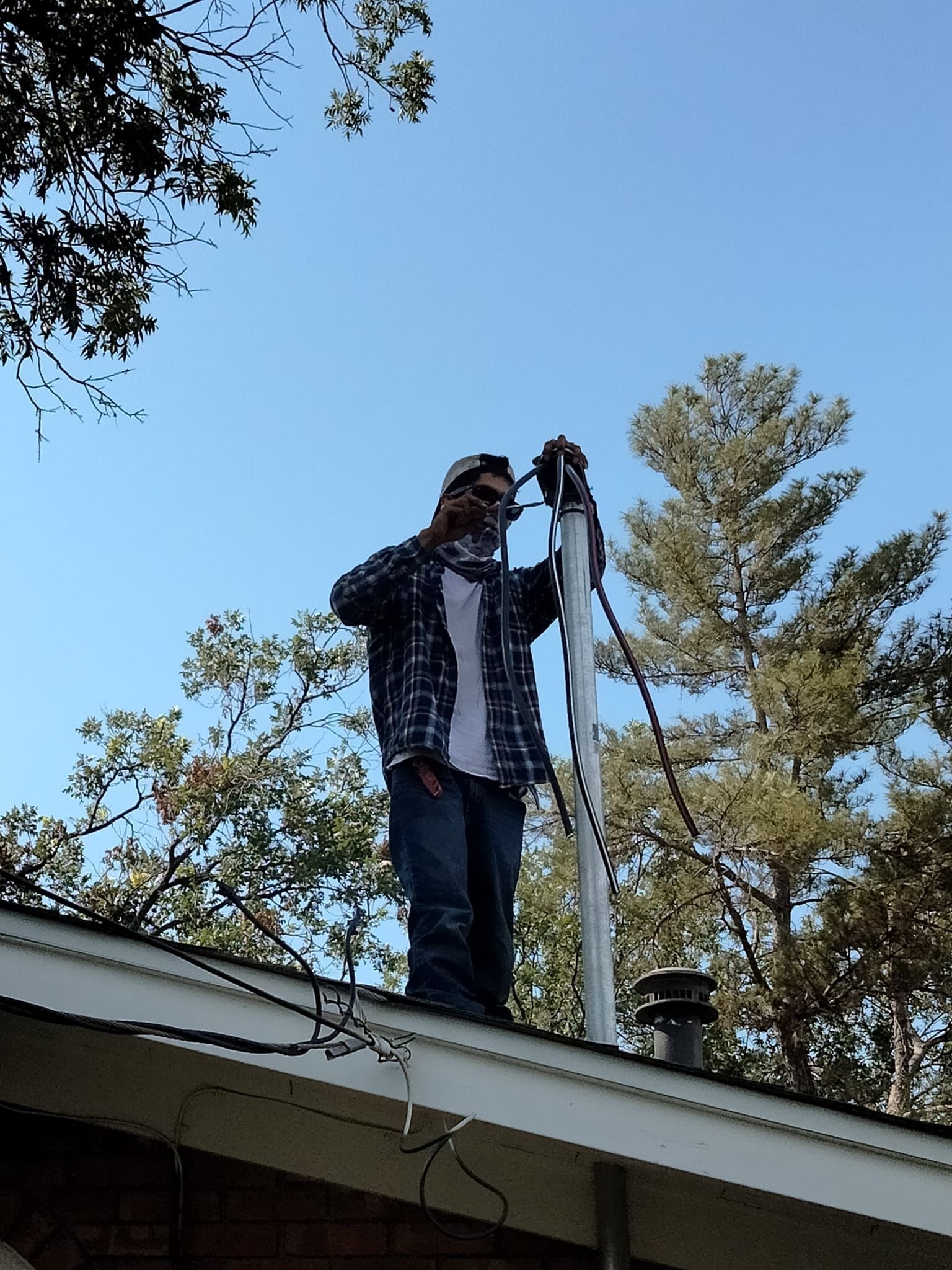A man in a plaid shirt is standing on the roof of a house