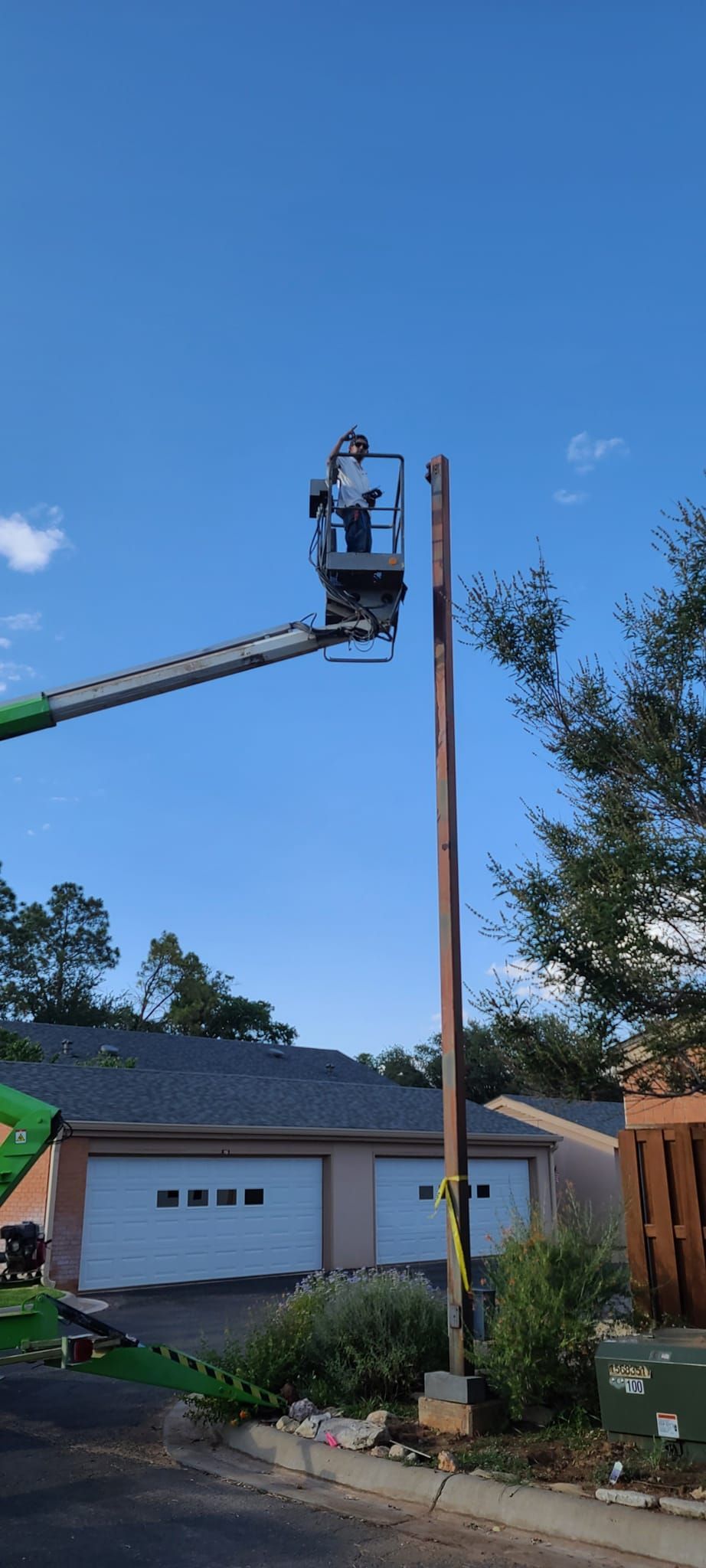 A man is sitting in a bucket on top of a pole.
