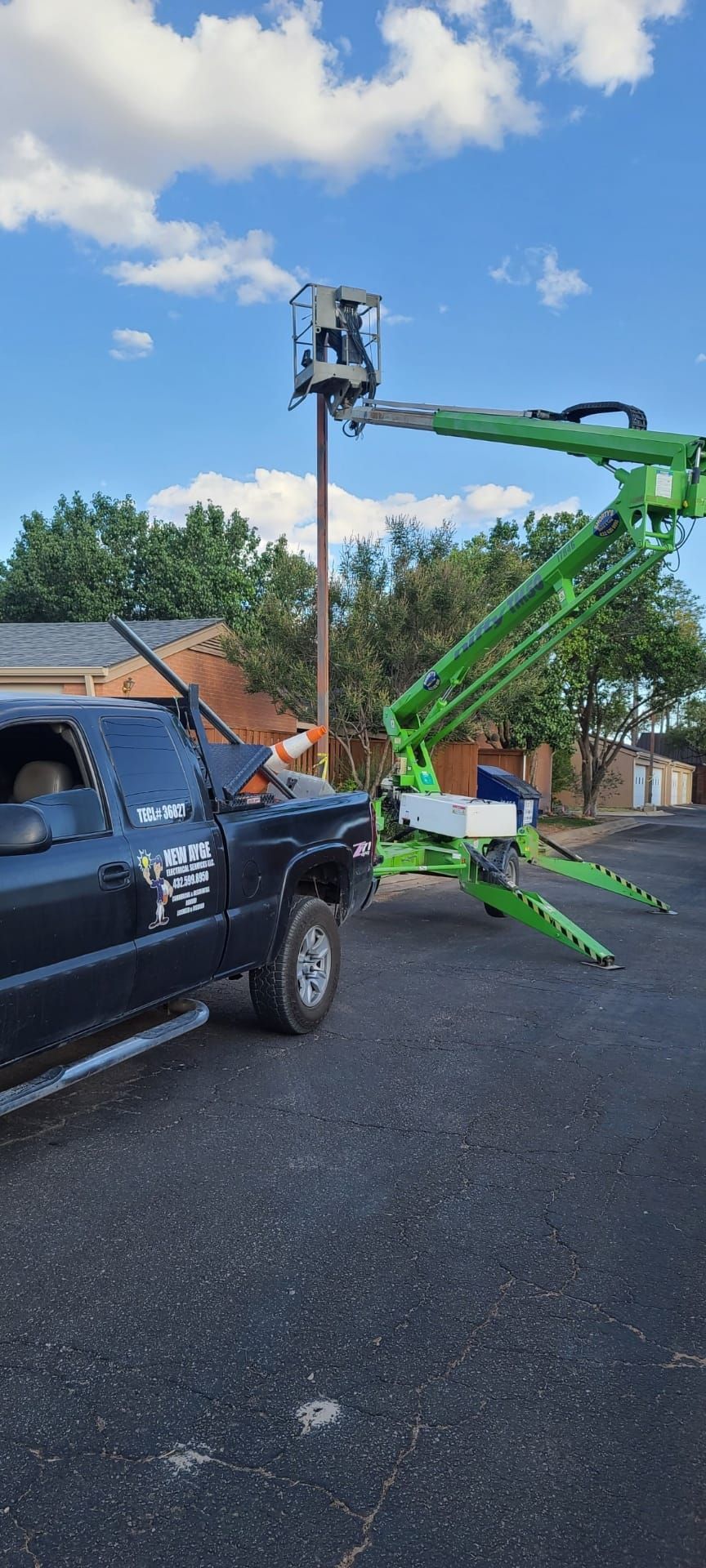 A truck is parked next to a green crane in a parking lot.