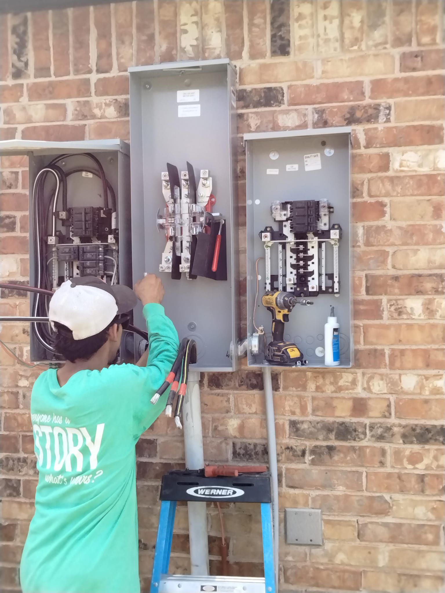 A man in a green shirt with the word dry on it is working on a electrical box on a brick wall.