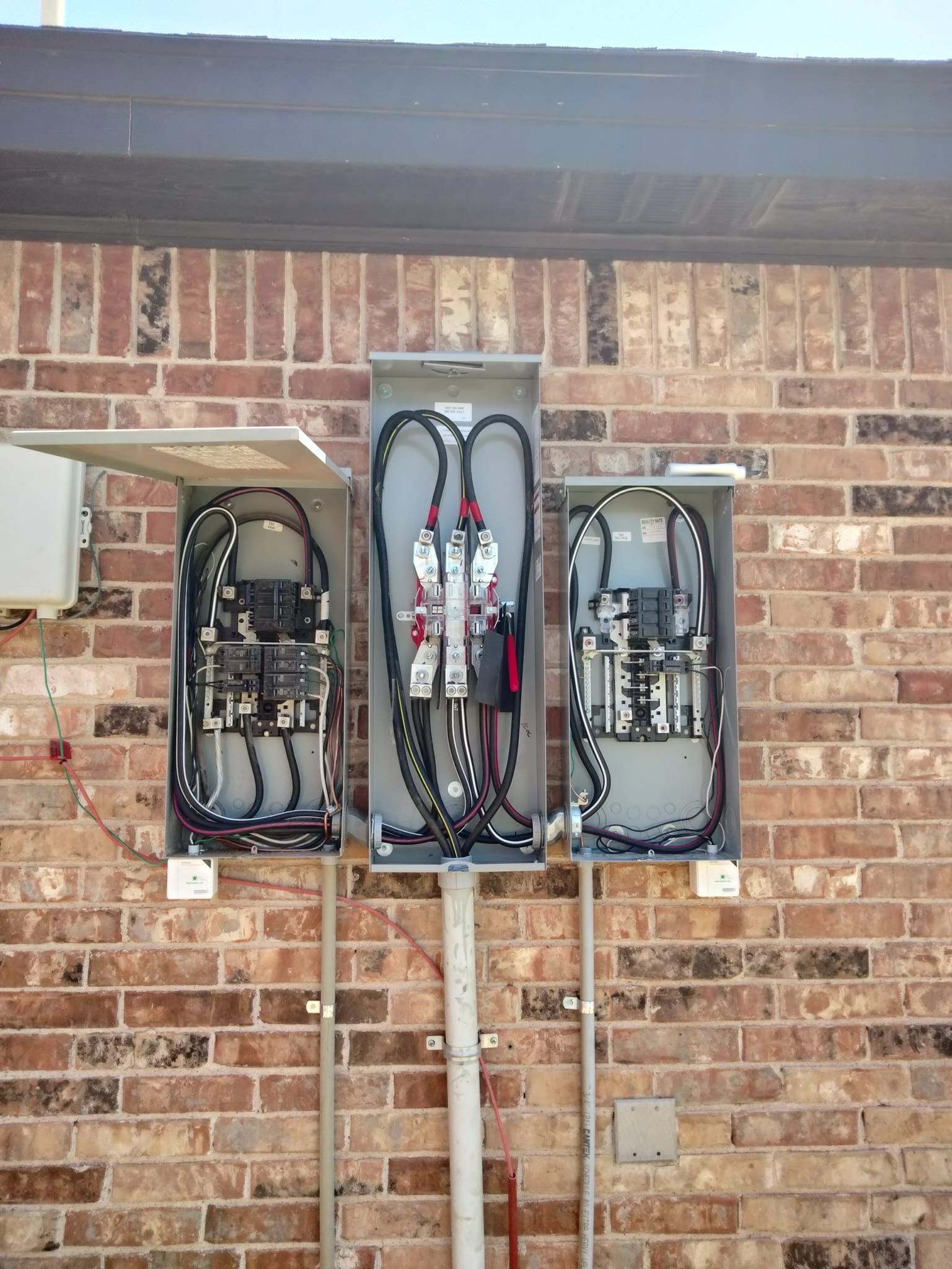 Three electrical boxes are sitting on a brick wall.