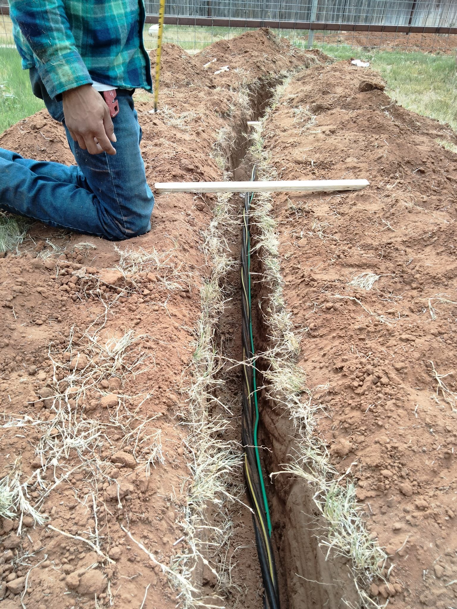A man is kneeling in the dirt next to a pipe.