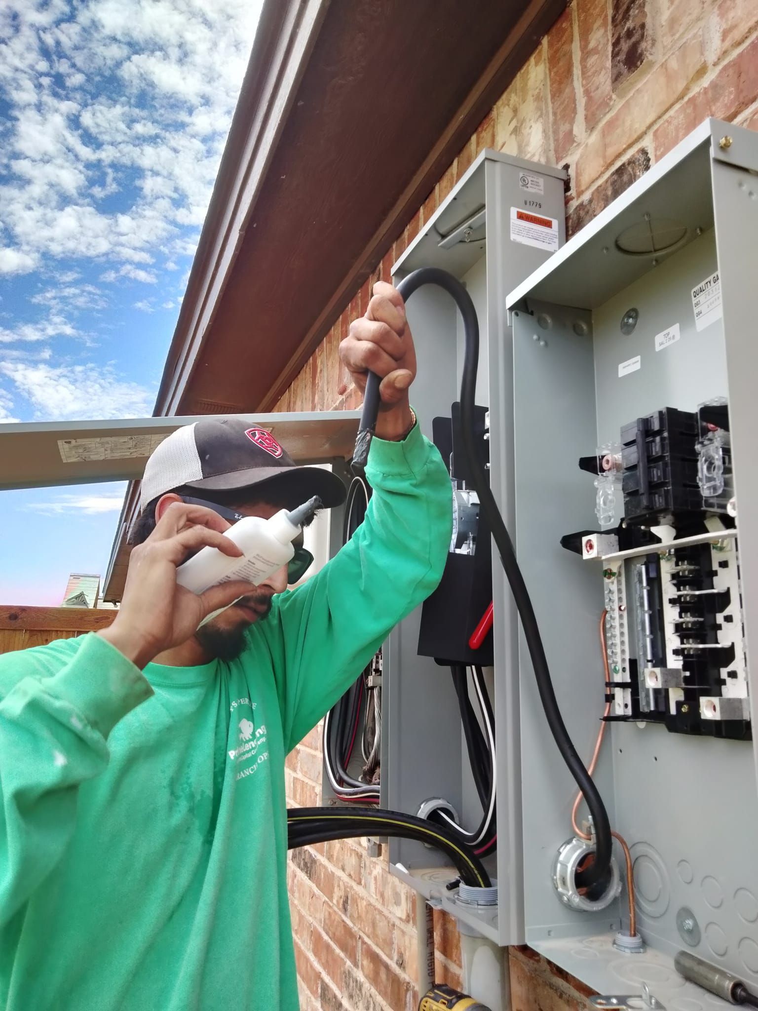 A man in a green shirt is working on an electrical box on a brick wall.