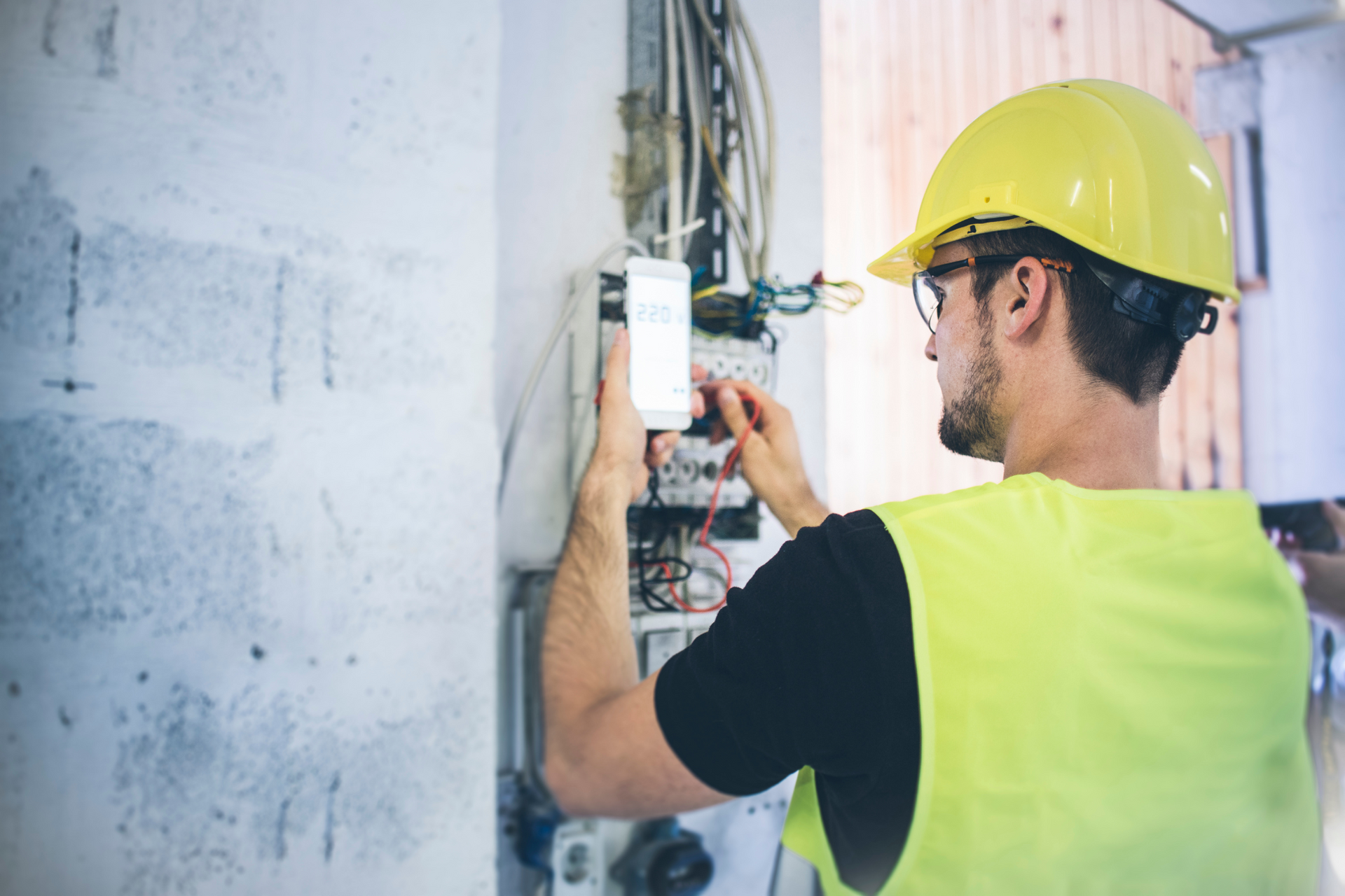 A man wearing a hard hat and safety vest is working on an electrical box.