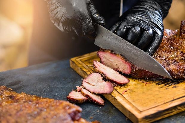 chef slicing smoked meat on wooden cutting board