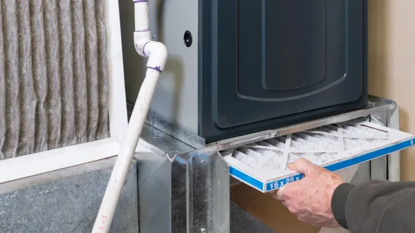 Person changing a furnace filter in a basement; filter is being pulled out.