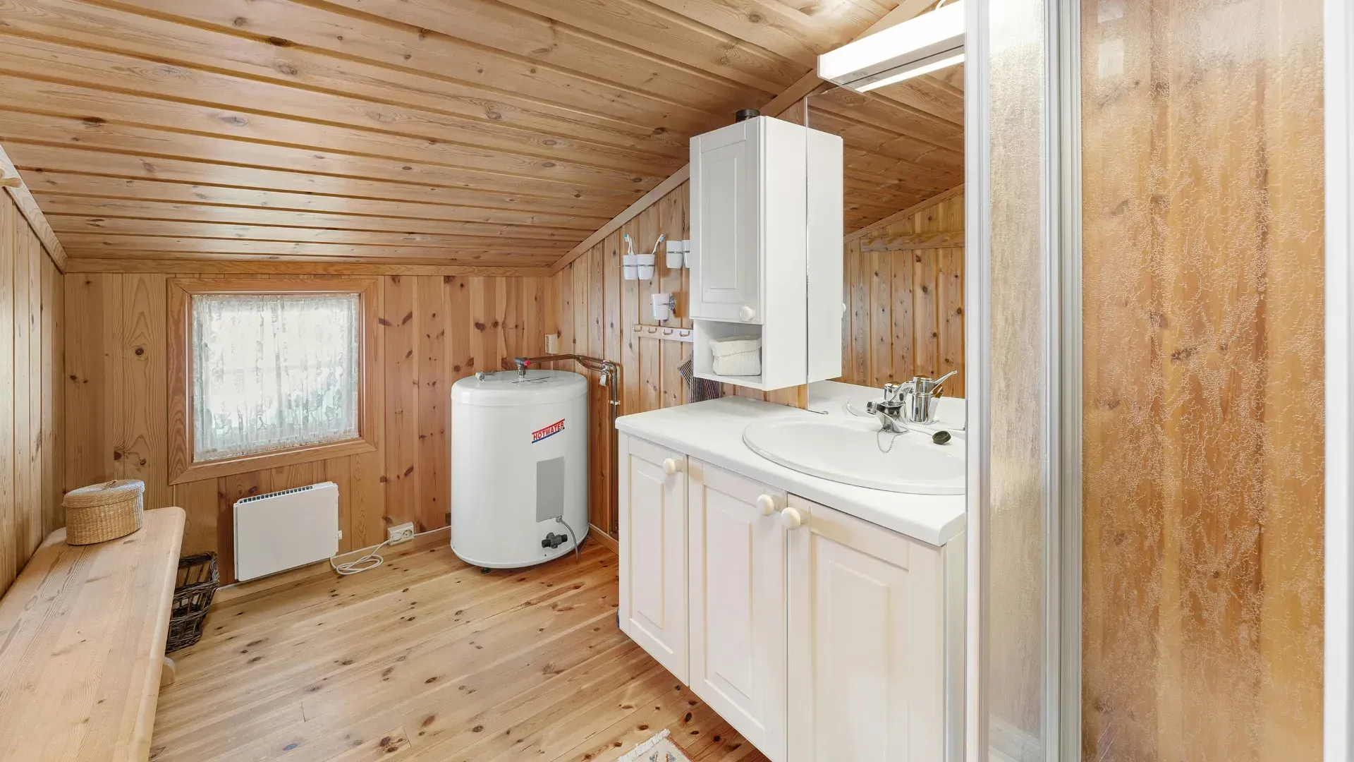 Small bathroom with wood paneling, white sink and cabinet, shower, and water heater.