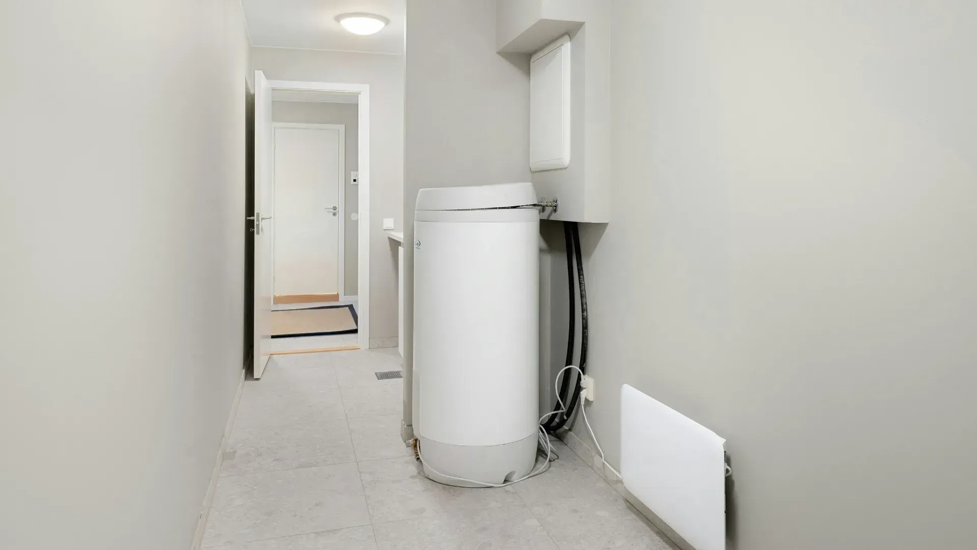 Narrow hallway with a washing machine, a white door, and a white wall heater.