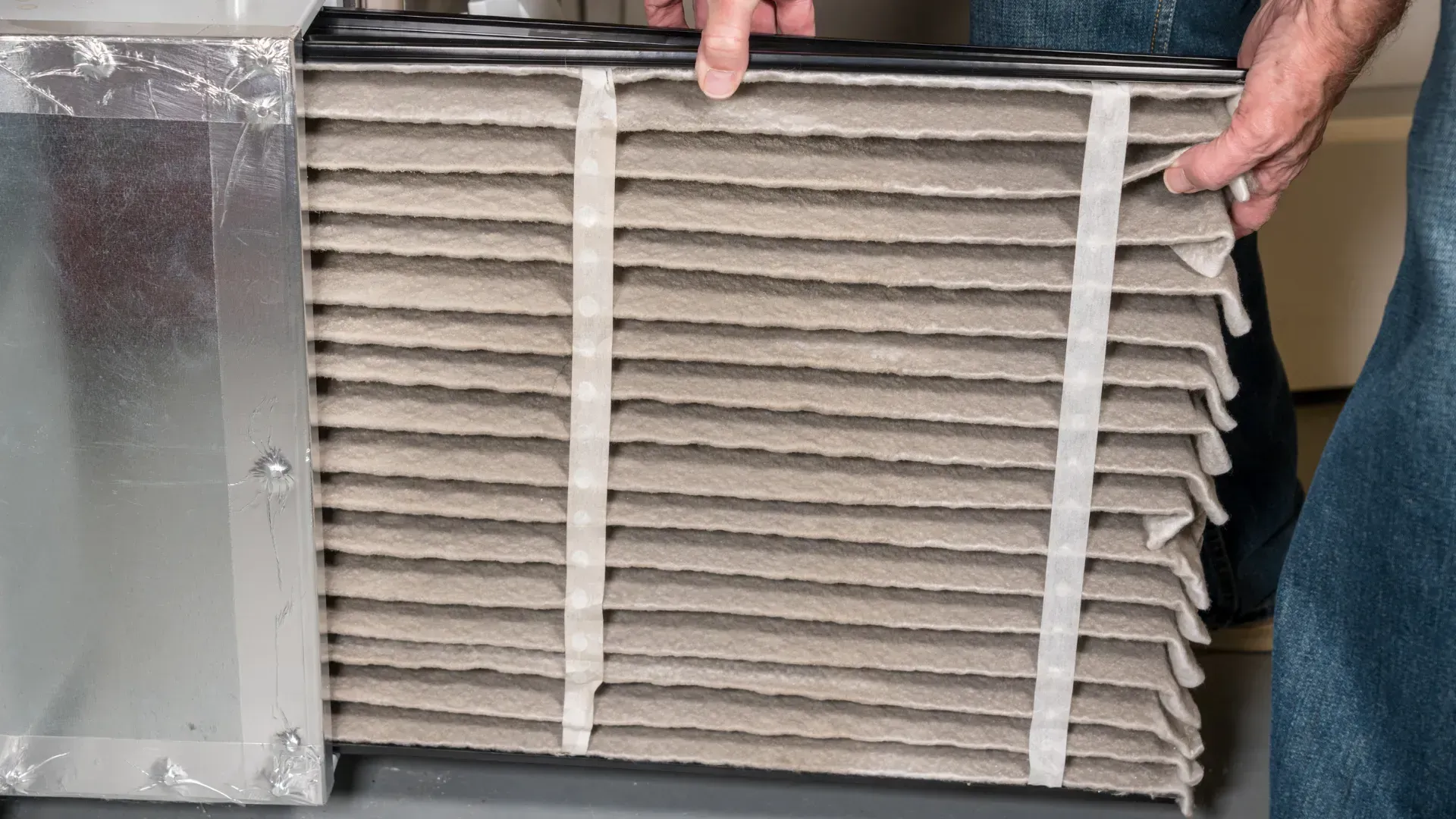 A person holding a dirty, pleated air filter next to a duct.