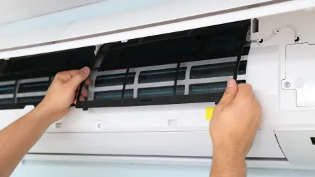Hands removing an AC filter from a white wall-mounted unit.