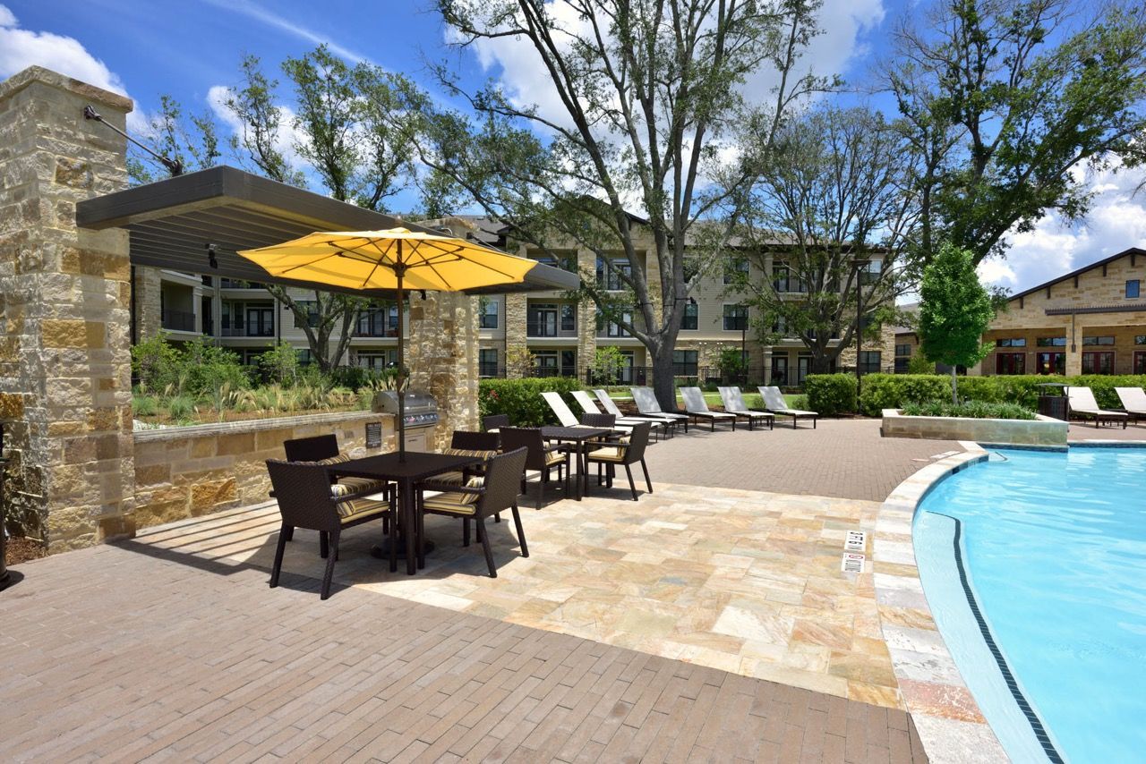 Outdoor apartment community pool area with lounge chairs, tables, and a yellow umbrella at Olympus Falcon Landing.