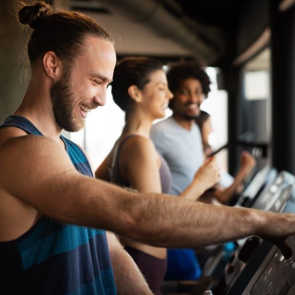 People in a gym smiling while exercising on treadmills.
