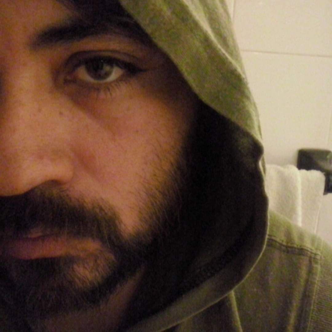 Hombre que lleva una sudadera con capucha verde mirando hacia la cámara con barba.