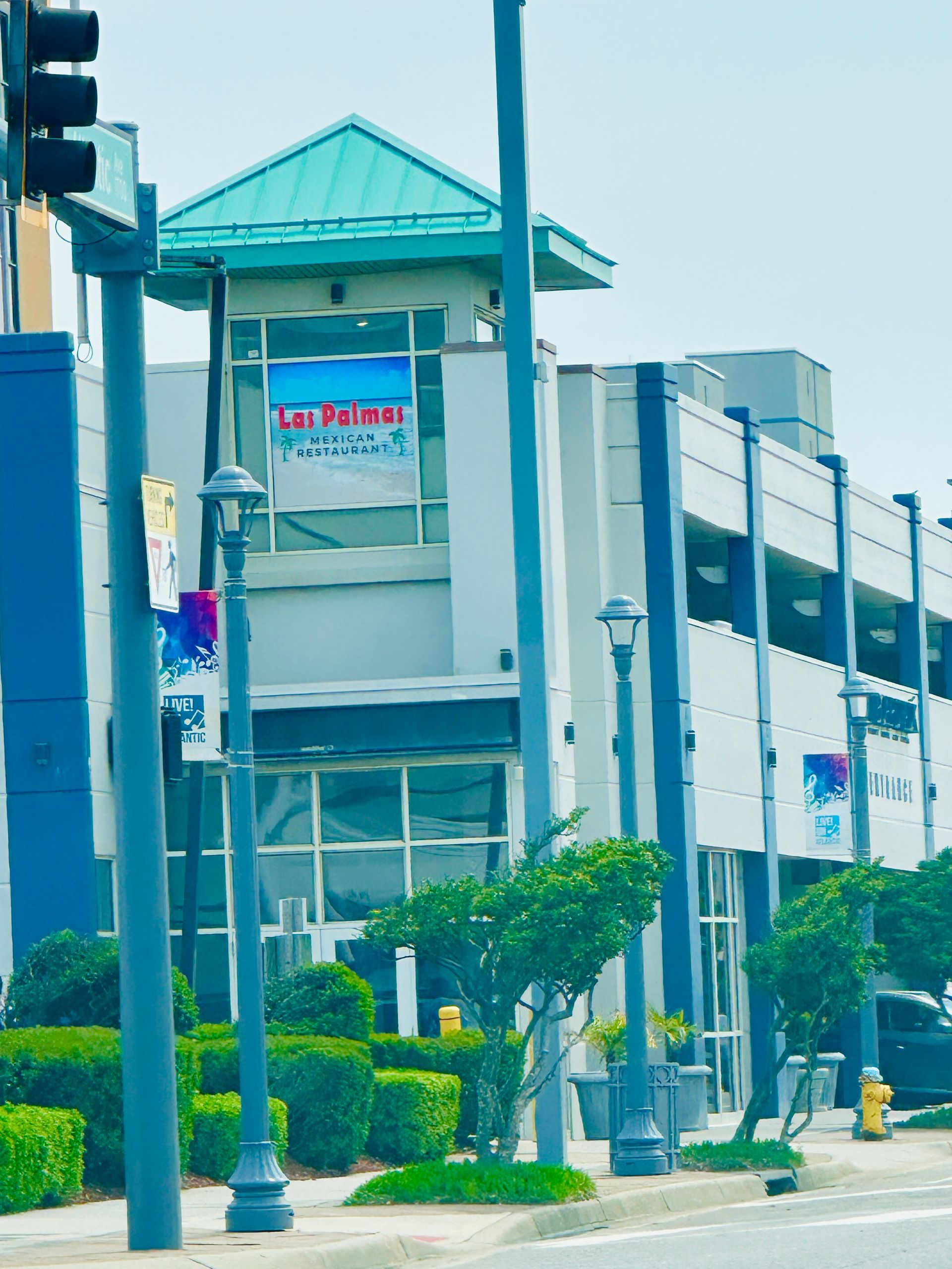 Multi-story building with teal roof and signage, street lights, and greenery.