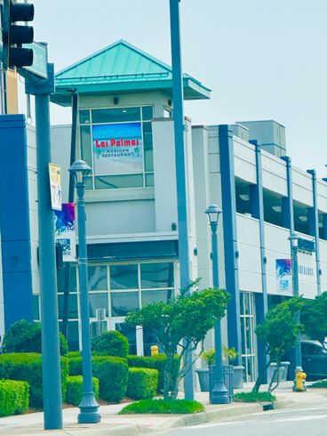 Multi-story building with teal roof and signage, street lights, and greenery.