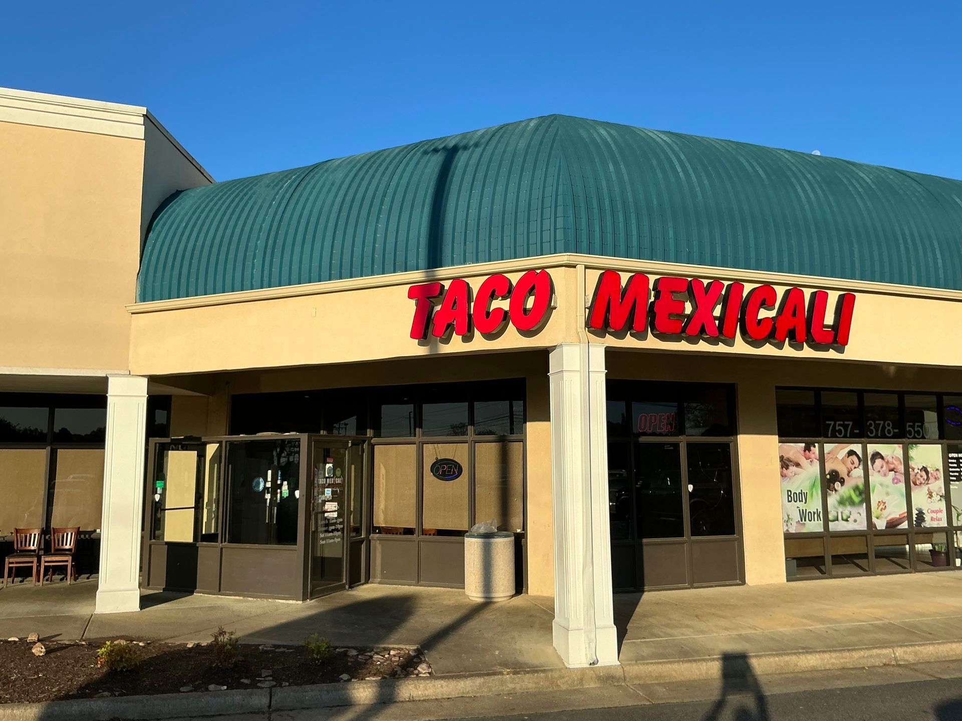 Taco Mexicali restaurant with a teal roof and a red sign, in a strip mall.