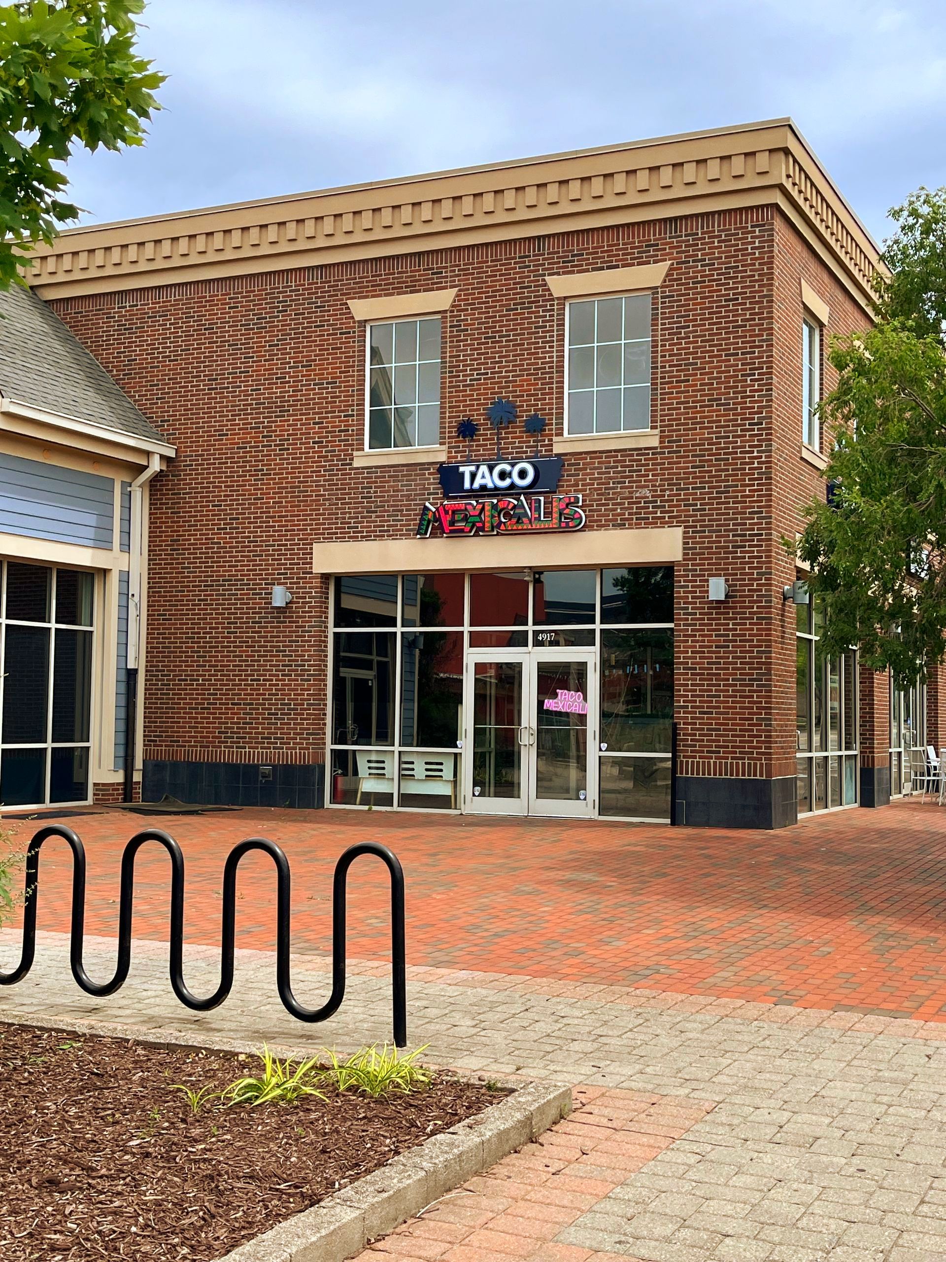 Taco Loco restaurant in a two-story brick building with a glass entrance, bike rack in front.
