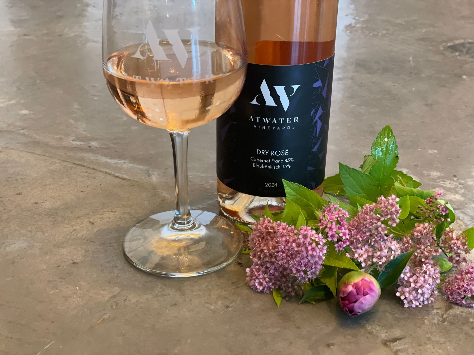 A glass and bottle of rosé wine with flowers on a gray surface.