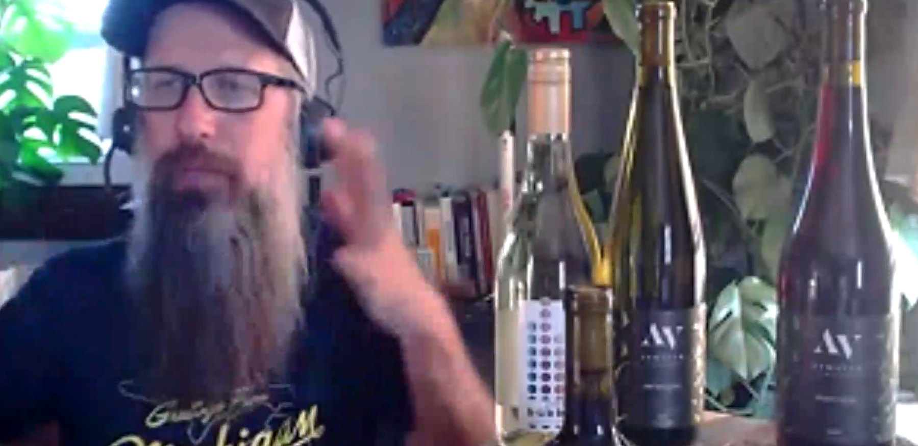 Man with glasses and a long beard speaking beside wine bottles