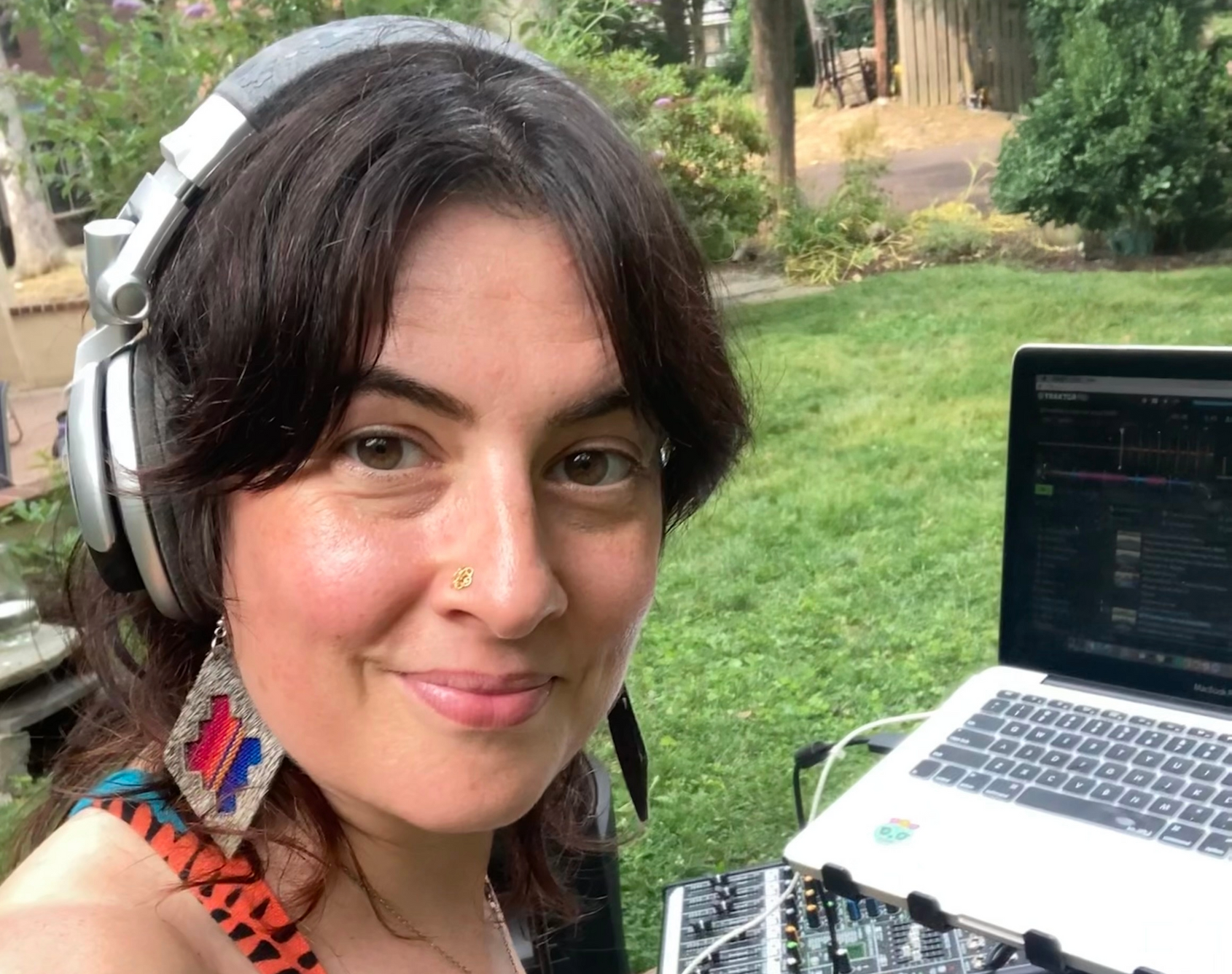 Smiling person wearing headphones beside a laptop outdoors in a garden