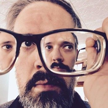 Man holding glasses, his face reflected multiple times.