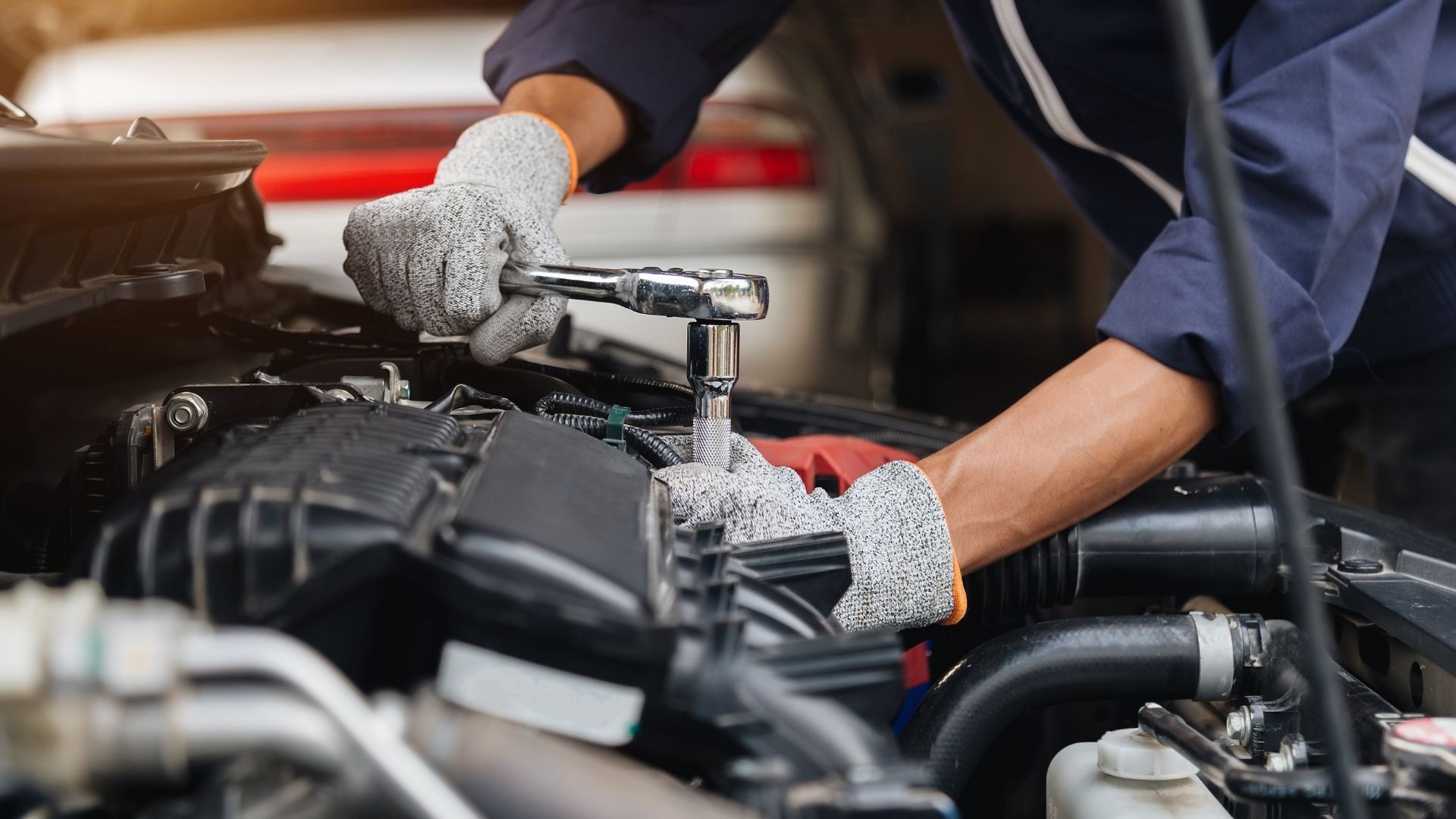 A mechanic is working on a car engine with a wrench.