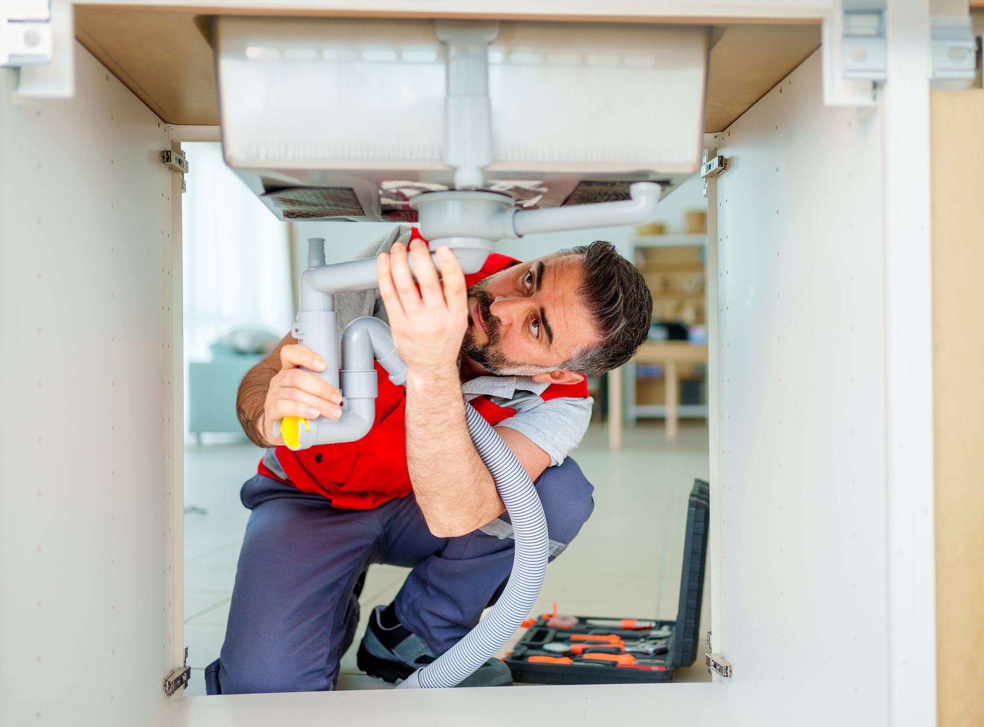 Ken Leonard Plumbing specializes in drain repairs and checkups, showing a male plumber fixing a sink’s drain.