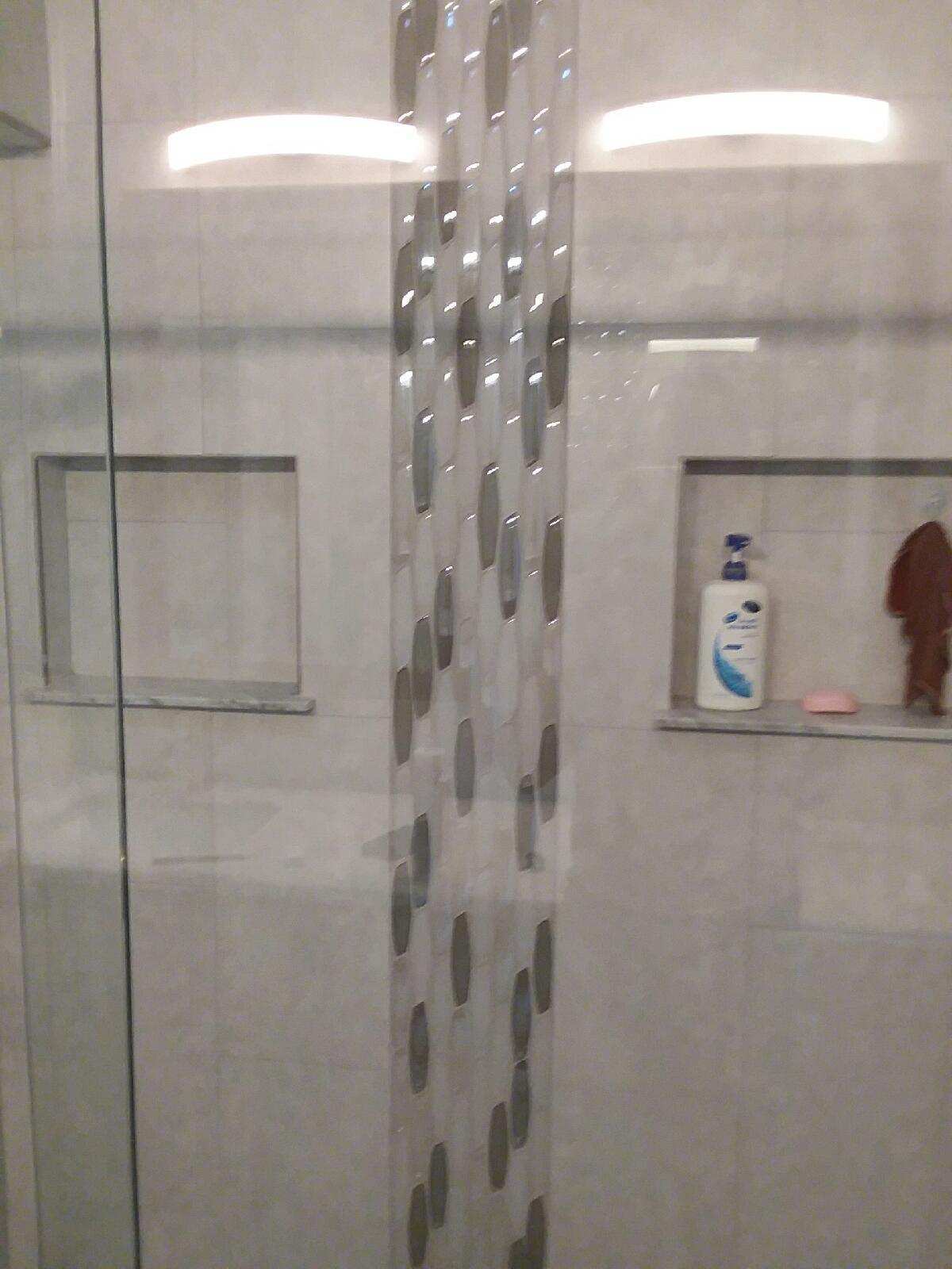 A shower stall with a bottle of dove soap on the shelf.