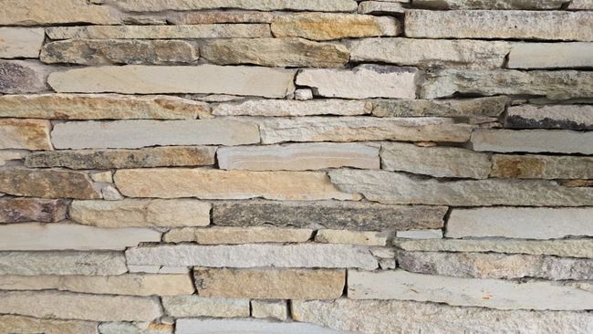 Primer plano de un muro de piedra apilada con rocas en capas de color beige y gris.