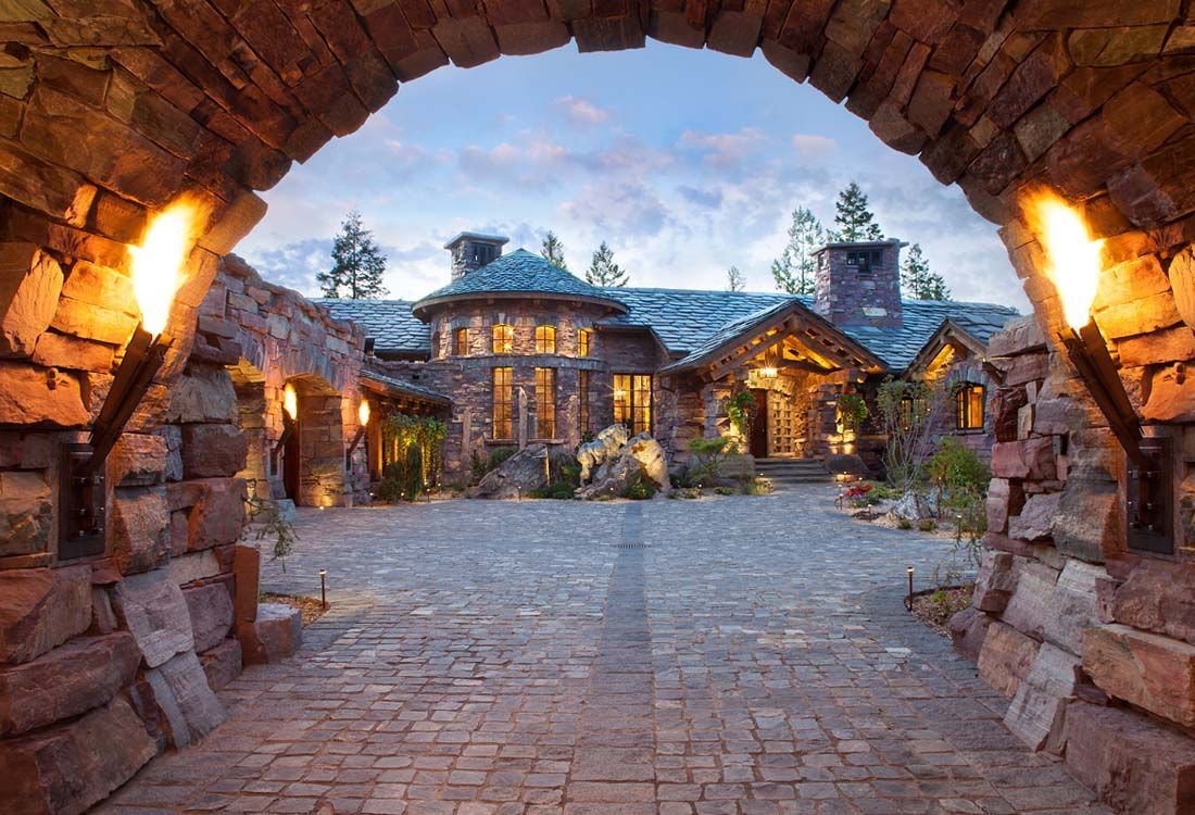 A stone archway leading to a large house.