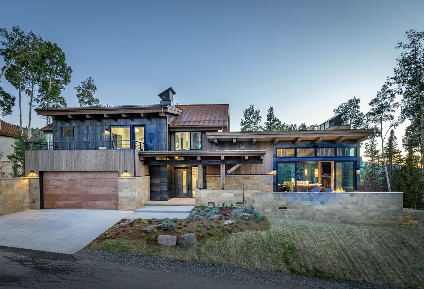 A large house with a large garage is sitting on top of a hill surrounded by trees.