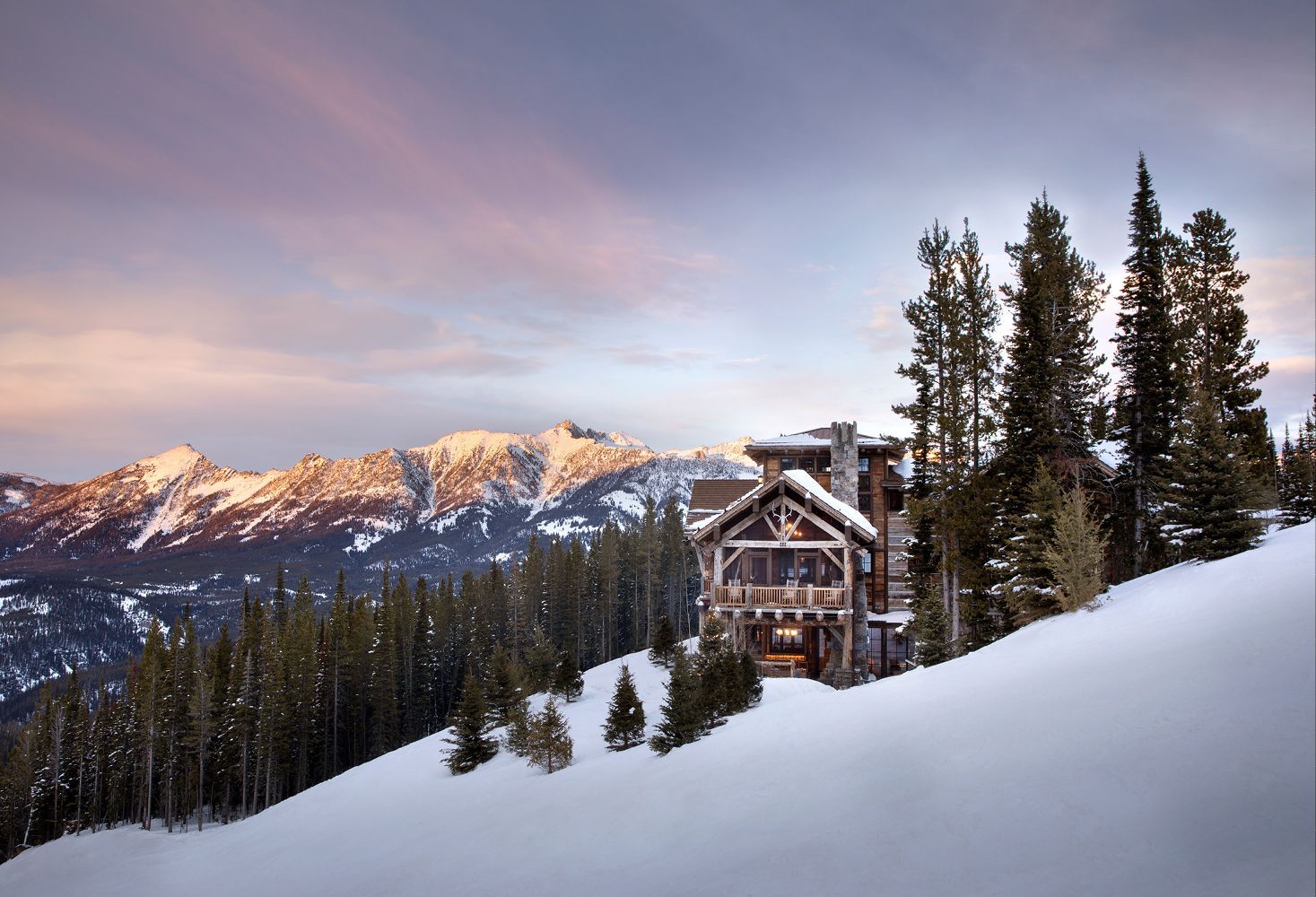 A snowy mountain with trees and a house in the foreground