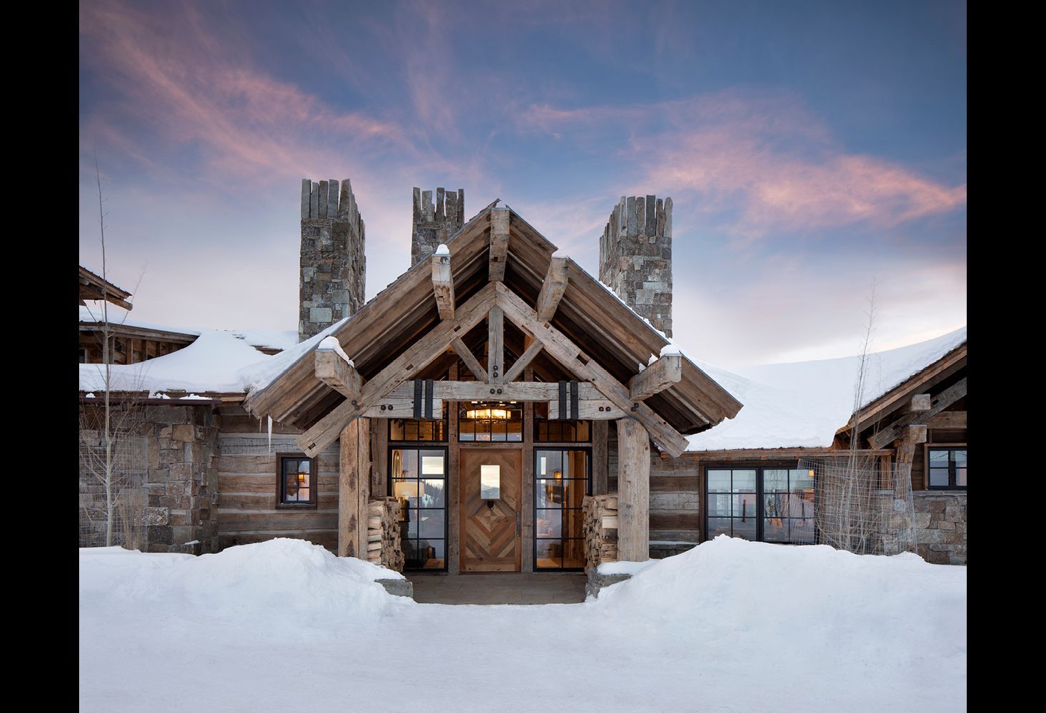 The front of a log cabin covered in snow.