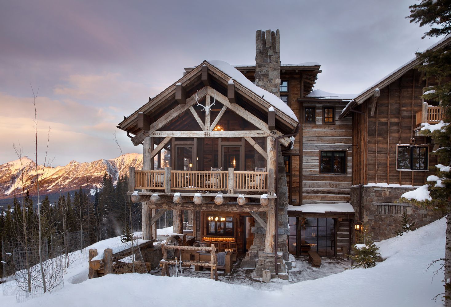 A large log cabin in the snow with mountains in the background