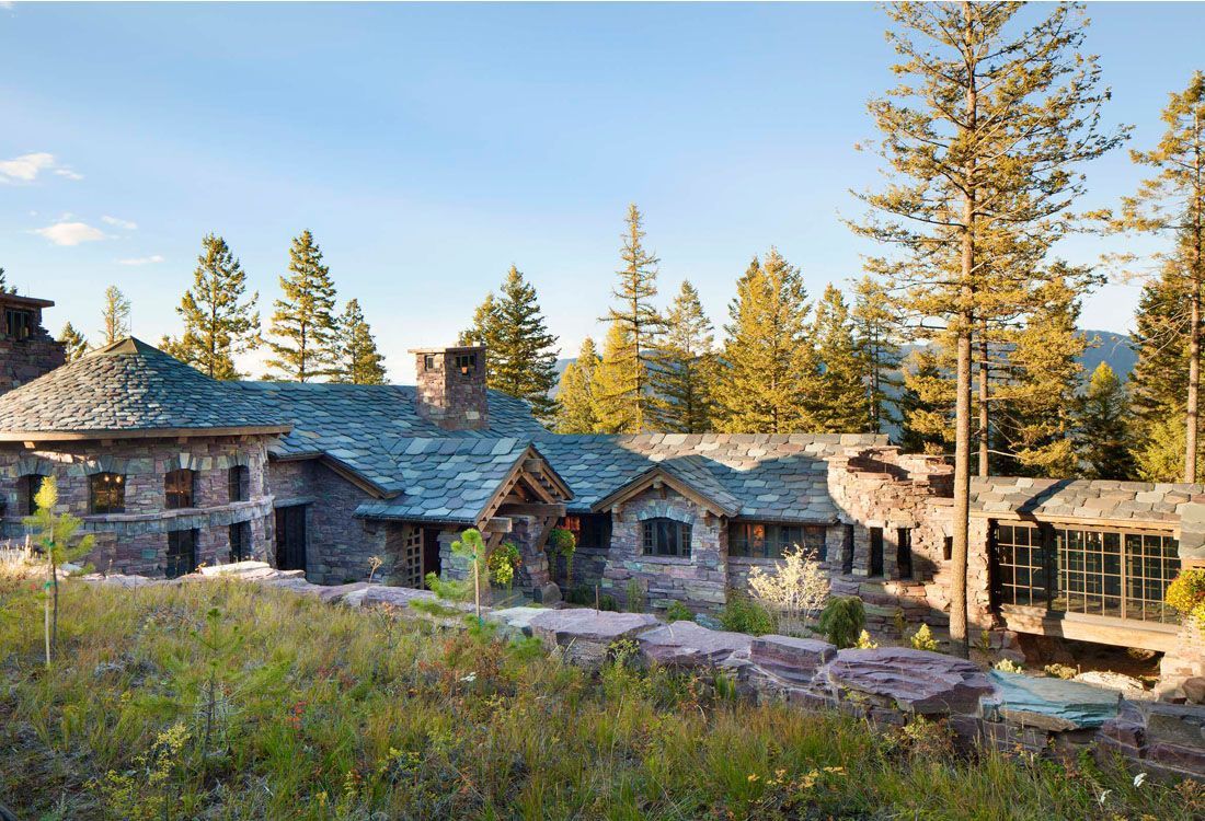 A large house with a blue roof is surrounded by trees and grass.