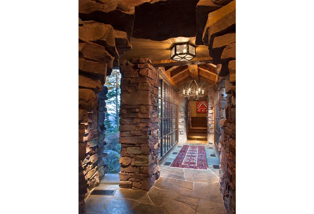 A long stone hallway with a chandelier hanging from the ceiling.