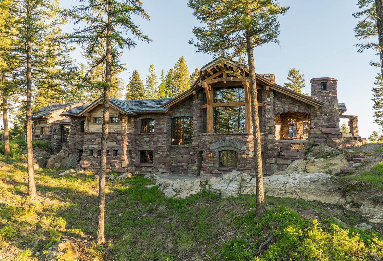 A large stone house is surrounded by trees on a hill.