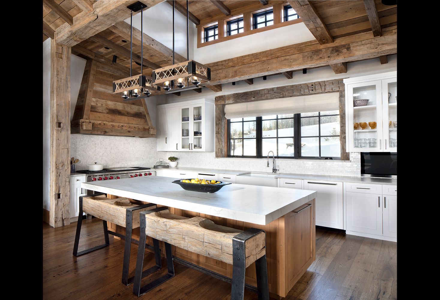 A kitchen with a large island , white cabinets , and wooden beams.