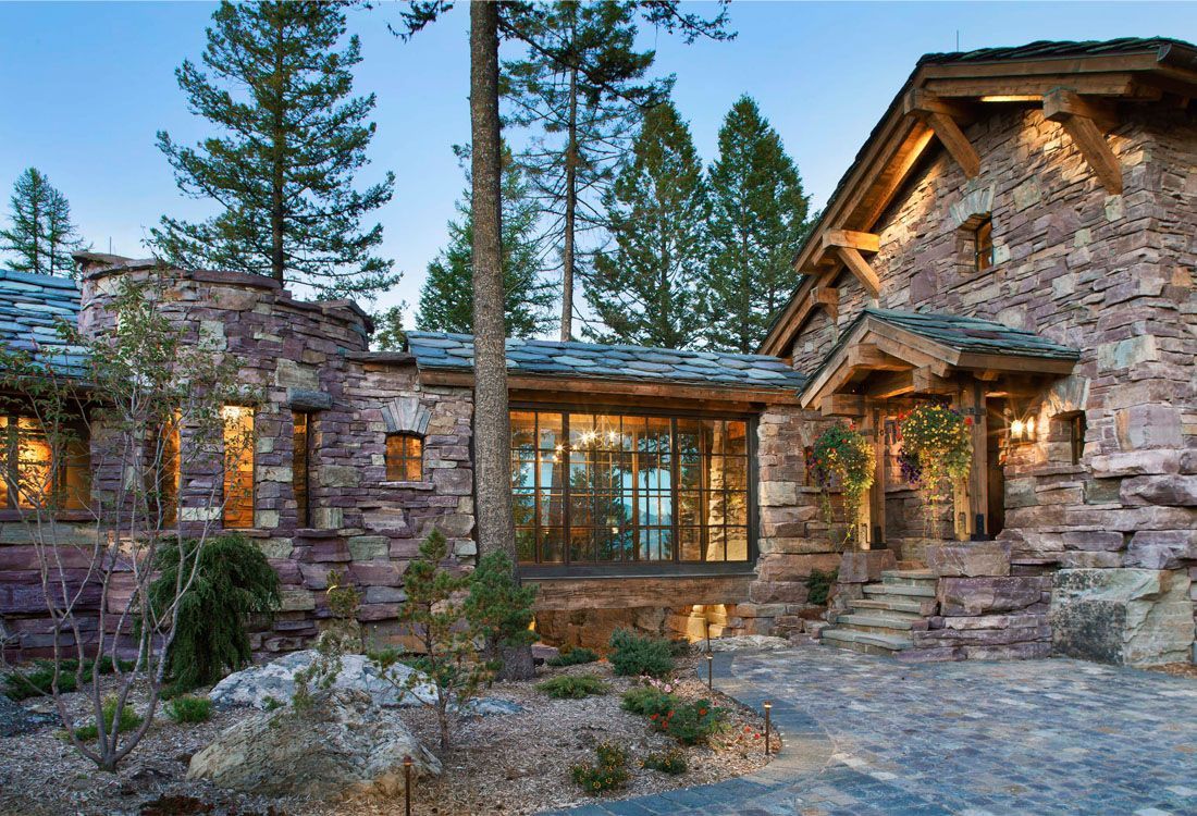 A large stone house with a wooden roof is surrounded by trees.