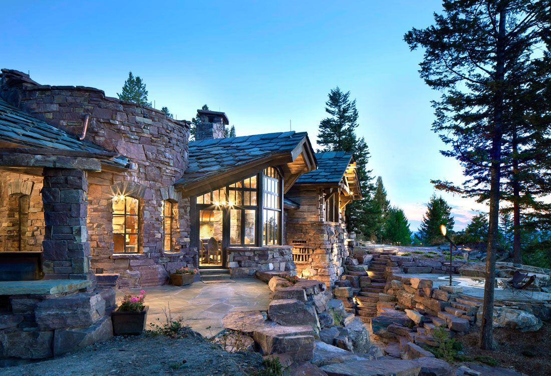 A large stone house with a lot of windows is surrounded by trees.